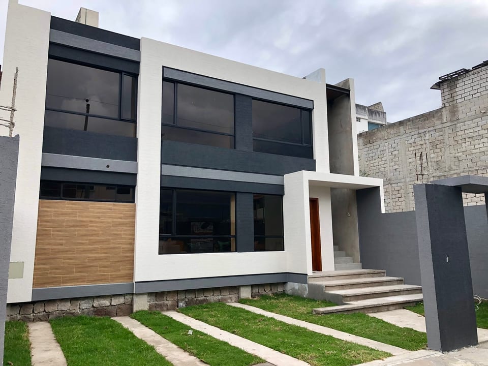 Vivienda de dos plantas terminada, con fachada en blanco, gris y madera